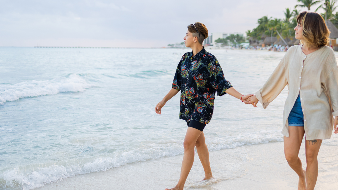 Same sex couple holding hands walking barefoot on a beach