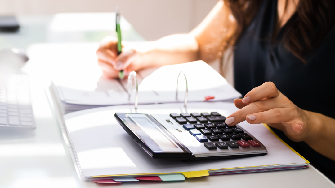 person using a pen writing with one hand and using a calculator with the other, taxes